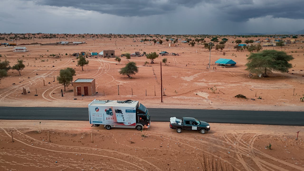 Home A scenic aerial view of vehicles on a road in a barren desert landscape, highlighting arid conditions.