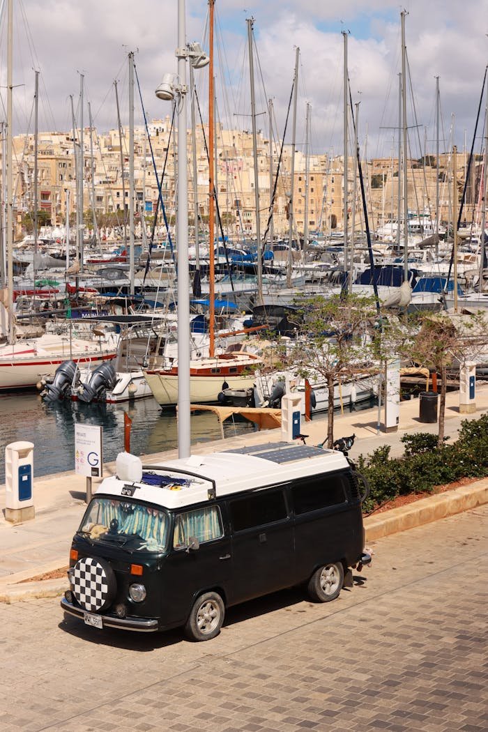 services-bg A black vintage van parked near the bustling marina in Birgu, Malta.