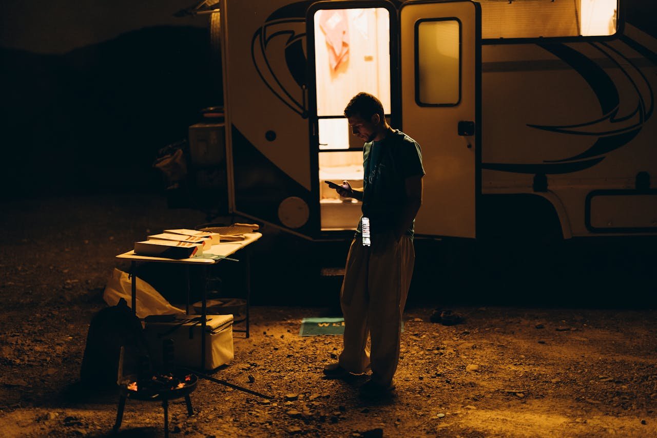 services-05 A moody nighttime scene of a camper using a phone outside a trailer in Showkah, UAE.