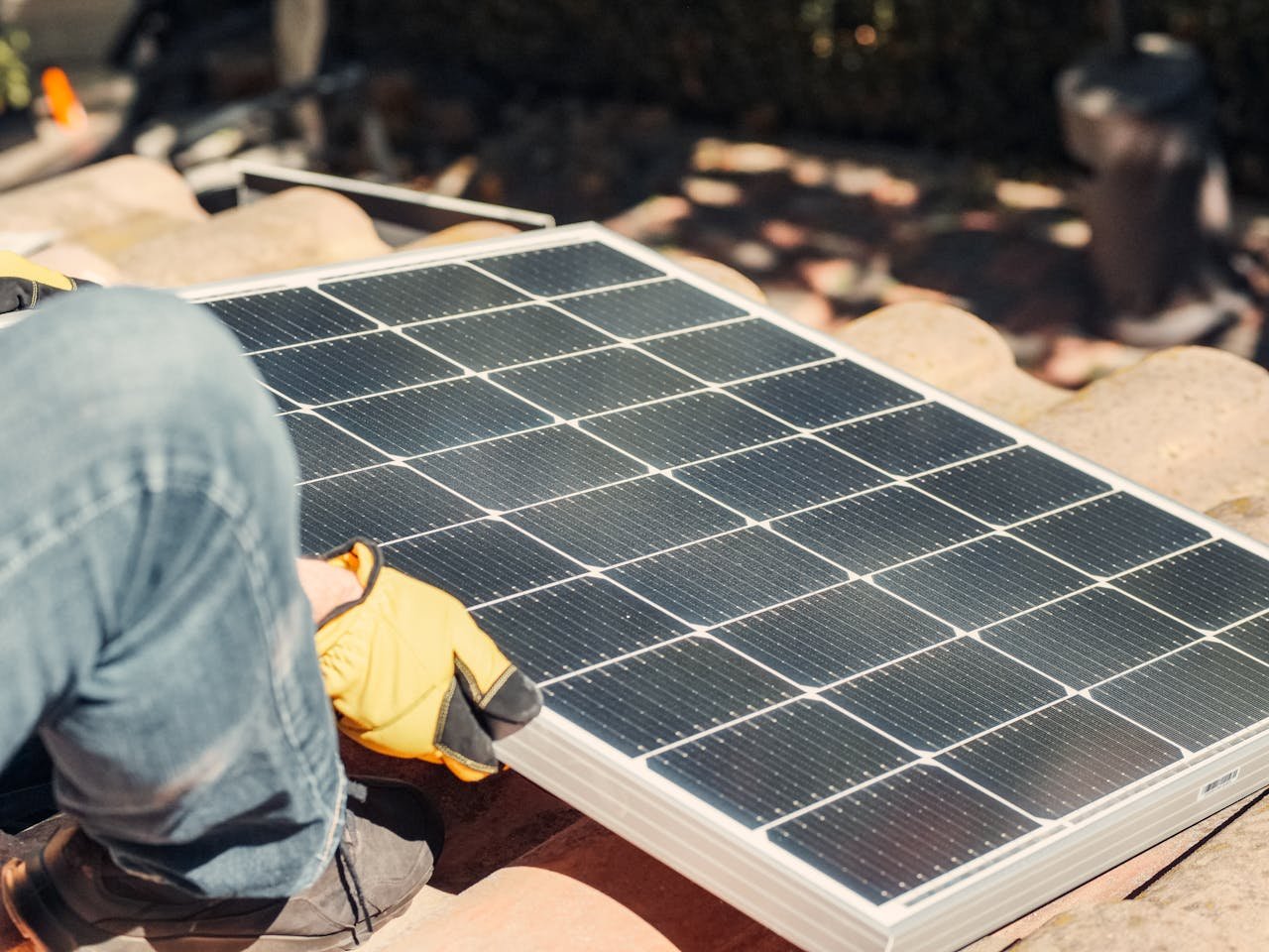 services-01 A worker installs a solar panel on a sunlit rooftop, exemplifying renewable energy.